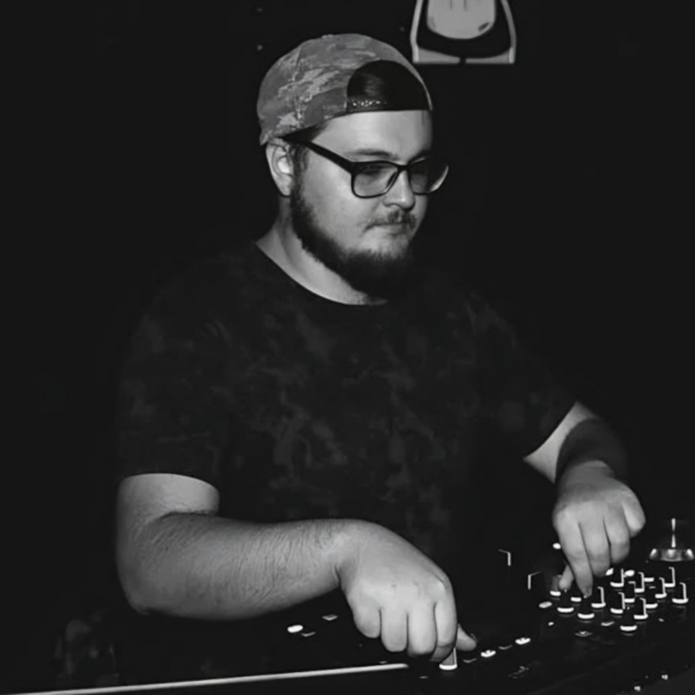 Black-and-white image of Andrés Moris wearing glasses and a backwards cap while adjusting controls on a DJ mixer, representing the Córdoba, Argentina DJ and producer known for Progressive House.