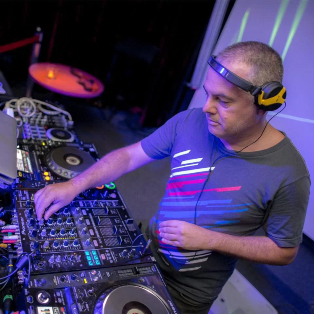 Marco Mei, Italian DJ and producer, working the Pioneer CDJs and mixer under purple club lighting, shot from above.Marco Mei, Italian DJ and producer, working the Pioneer CDJs and mixer under purple club lighting, shot from above.