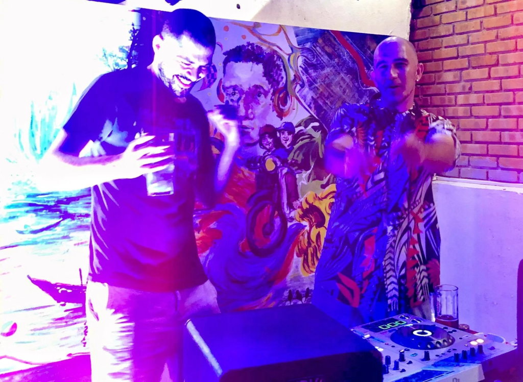 Romanian DJ Bipolar Bear and French DJ G Nomad Standing under UV light whilst performing as DJs, colour image.