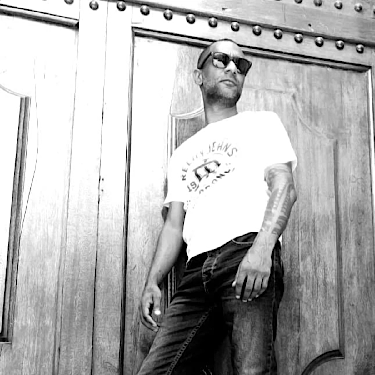 South African DJ and Producer Liquid Static Standing in front of door wearing sunglasse4s, black and white image.