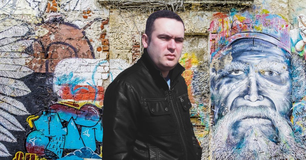 Portuguese DJ Joshua standing in front of a mural on a wall, colour image.