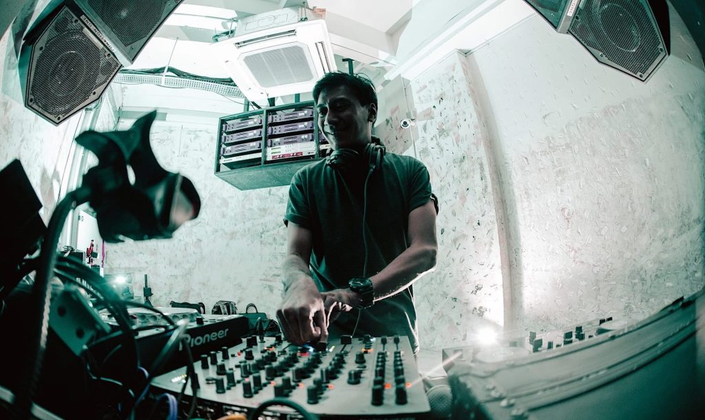 Brendon P smiles while performing behind a Pioneer DJ setup, representing his long-running work across Singapore’s club scene and international House music circuit.