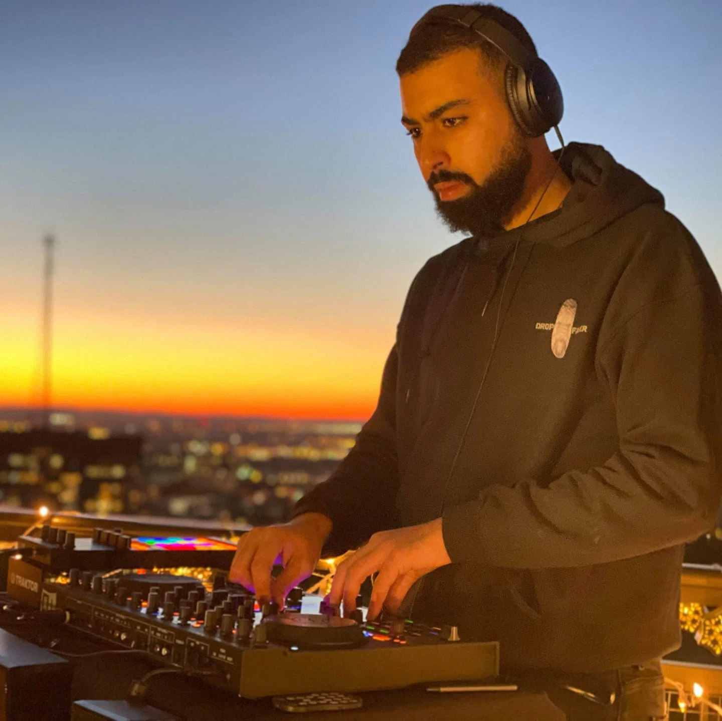 Moroccan Techno DJ Dropfader performs on a rooftop at sunset, representing his dark, acid-influenced rave sound and underground Techno style.
