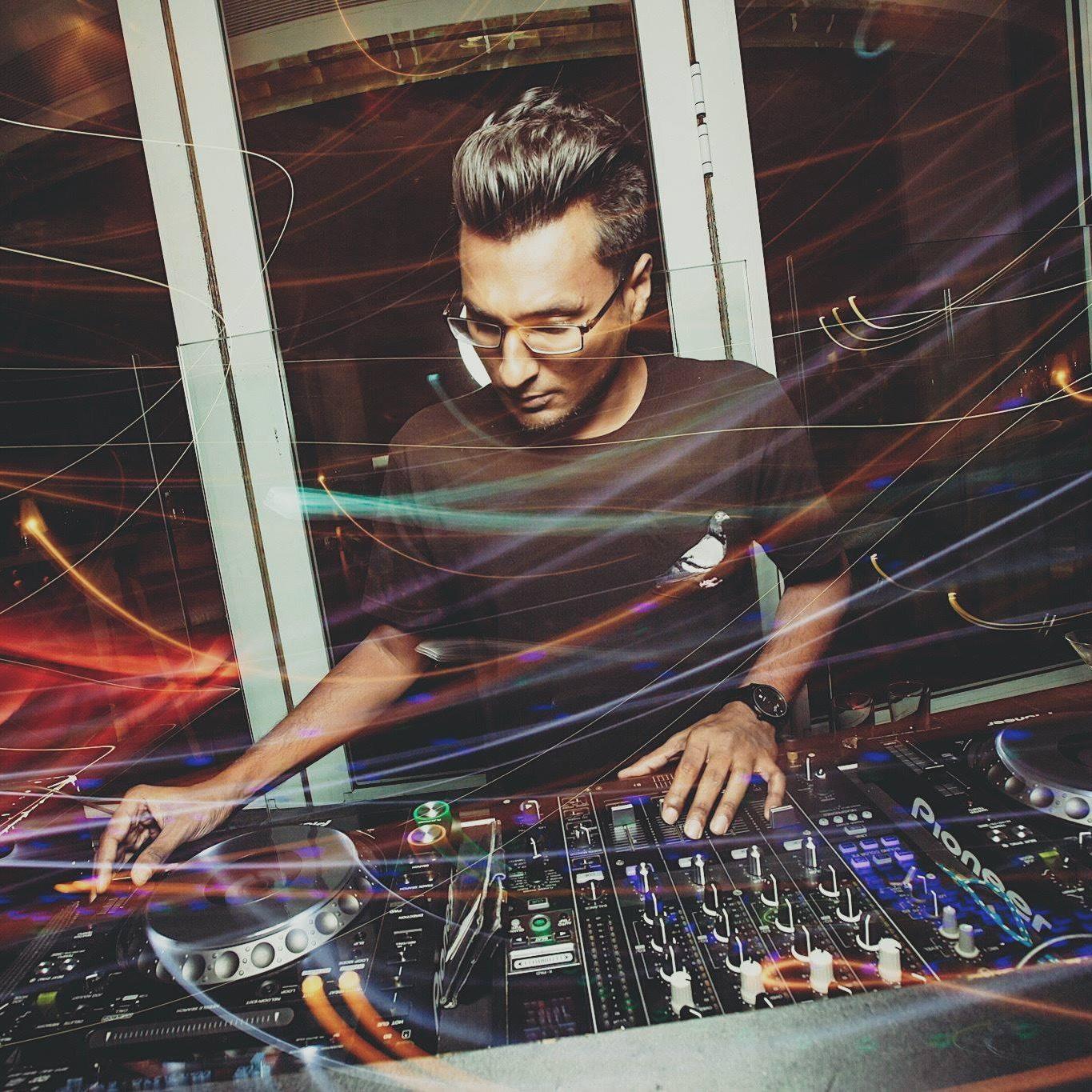 Singaporean DJ Sivanesh performing at a venue on Pioneers CDJs and DJM 900 Mixer, image taken in colour from front, many swirls of light.