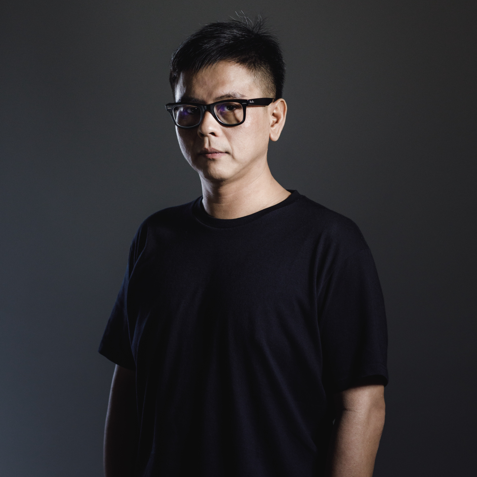 Malaysian DJ and producer Terence C standing with his hands in his pockets in a studio shot with the right side of his face in a shadow, colour picture.