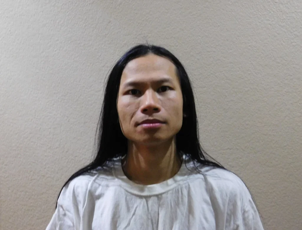 Colour portrait of Los Angeles DJ and producer 6047, also read as 60:47, facing the camera with long dark hair and wearing a white shirt against a plain textured wall.