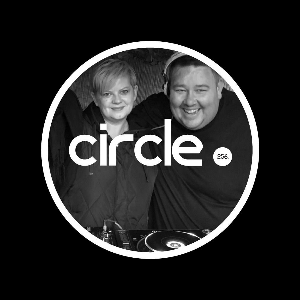 Rocka Lula and Robert Van Ryn standing behind circle. 256 logo