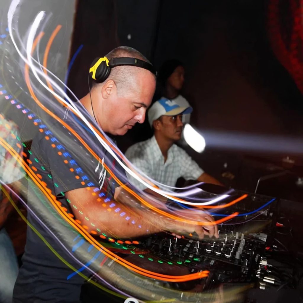 Marco Mei, Italian DJ and producer, focused at the mixer with long-exposure light trails swirling around him in a dark club setting.