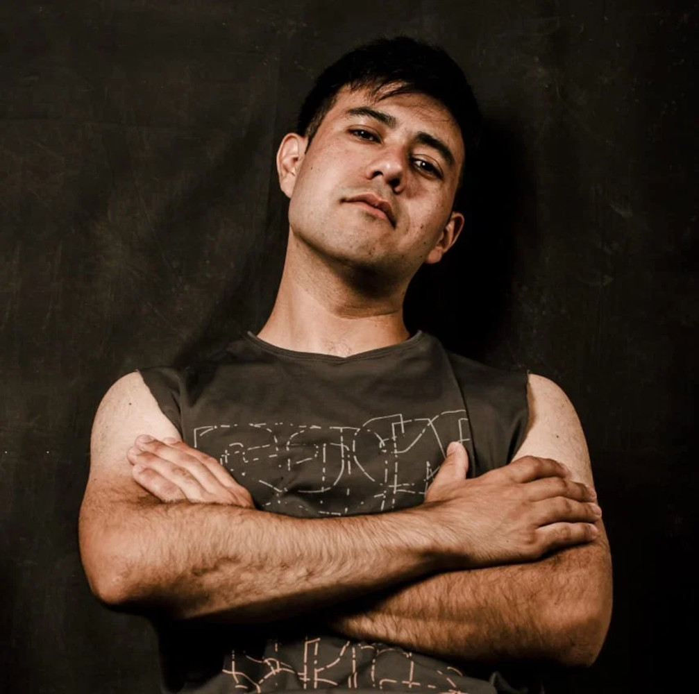 Portrait of Argentine DJ and producer Andhi Rivas standing with crossed arms against a dark studio background, representing his Progressive House and Techno sound.