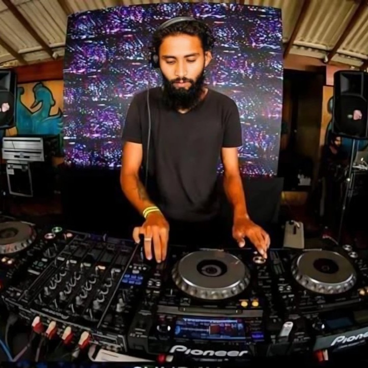 HarsH performing on Pioneer CDJs at an indoor venue, with a colourful LED screen behind him.