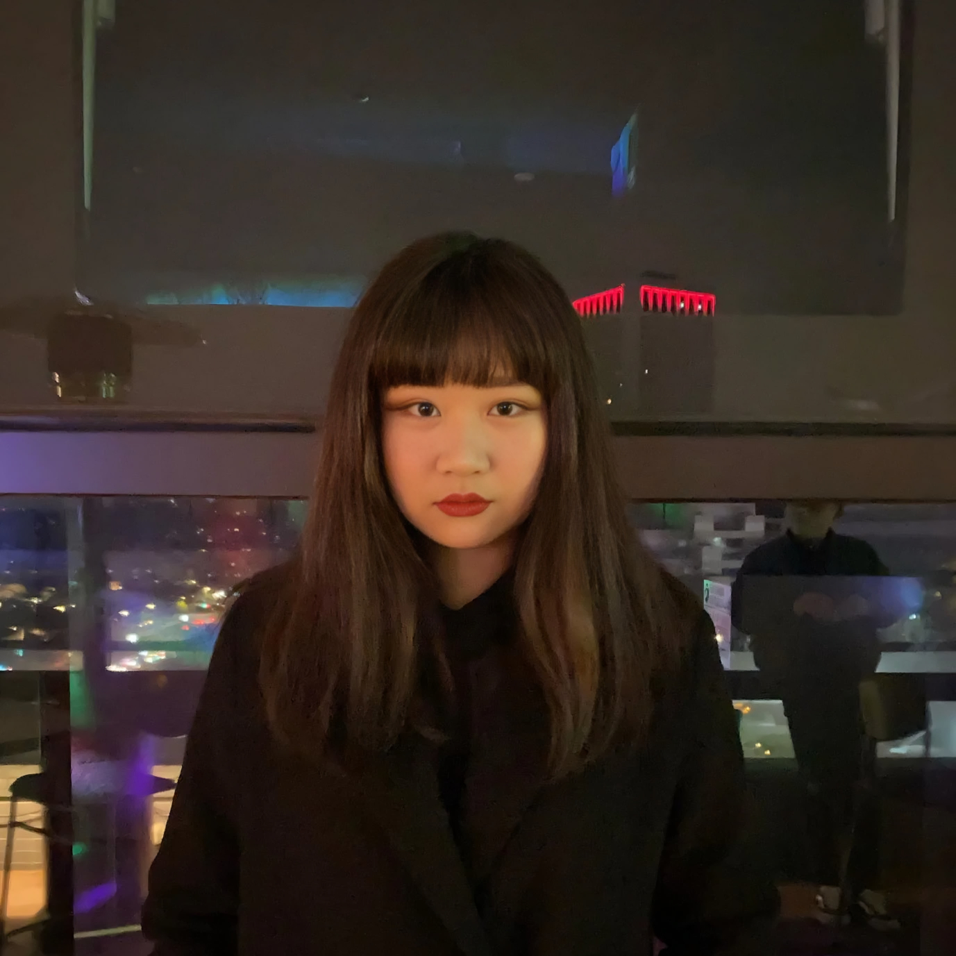 Portrait of Taiwanese DJ Venci standing in front of a night-time city view, representing her techno, psy, acid and leftfield electronic sound.
