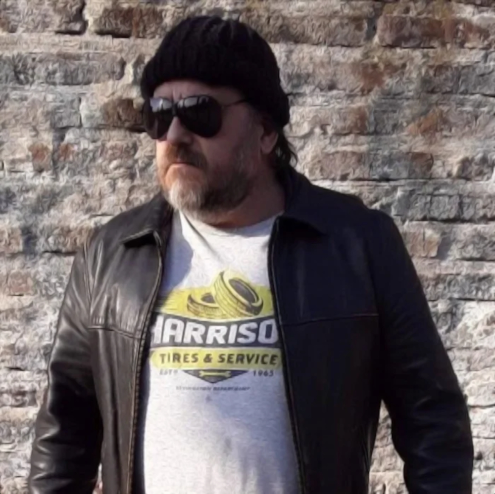 Argentinian DJ and producer Falso Simulacro wearing sunglasses, a Woolen Hat and a leather jacket in upper body shot, colour image.
