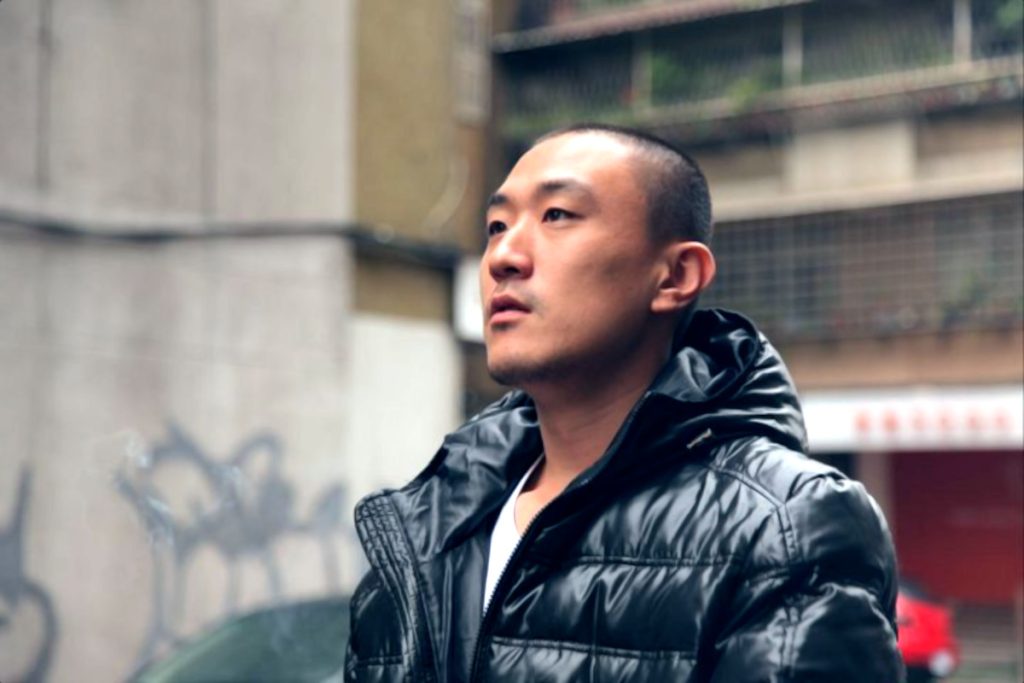 taiwanese DJ and Record label owner Murphy Kin looking Up standing in street, colour image.