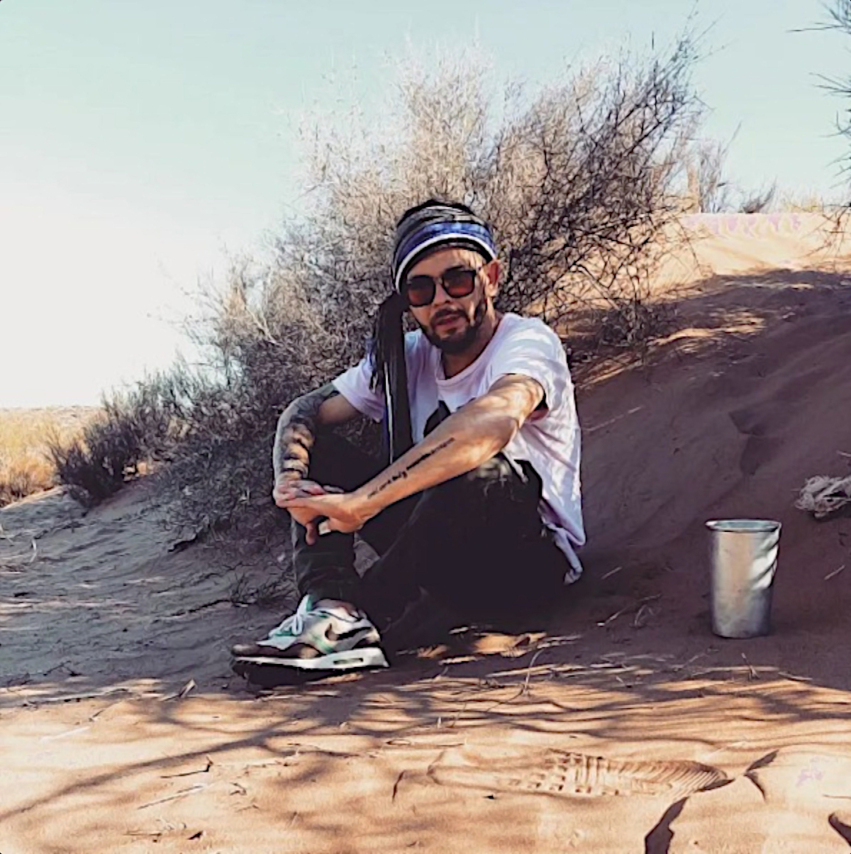 Argentinian DJ and producer Facucio sitting with elbows on knees in the Desert wearing sunglasses, colour image.