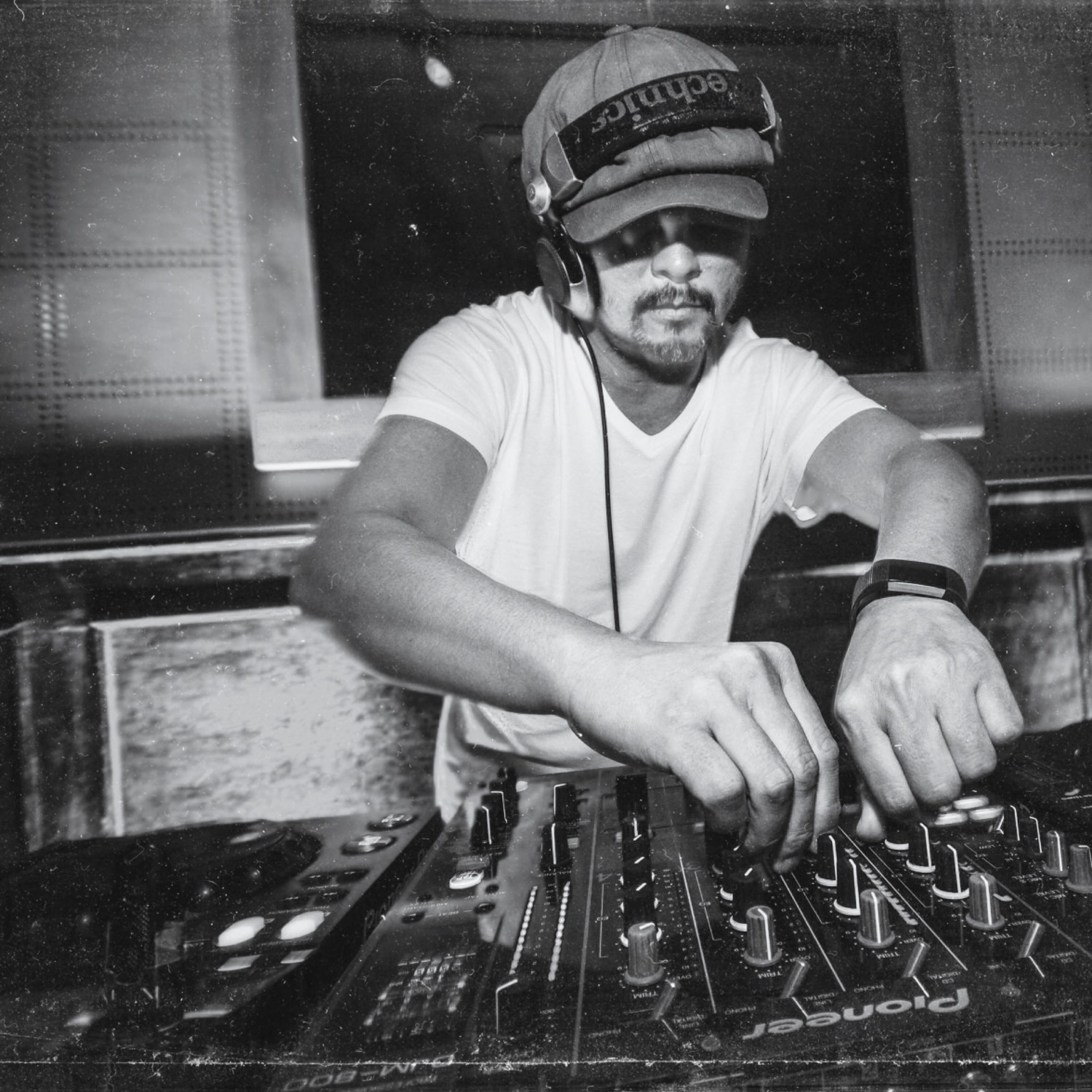 Filipino DJ and producer Herb cabral twidling knobs on Pioneer DJM Mixer wearing a hat and Technics Headphones, black and white image.