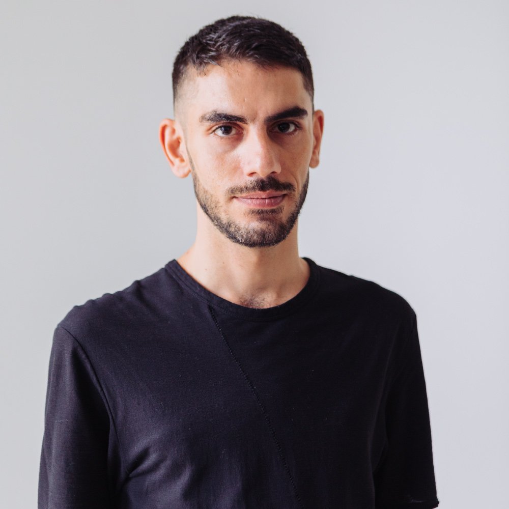 Malaysia-based Iranian DJ and producer Otherkind stands in front of the camera, gazing directly at it while wearing a black T-shirt in a color image.