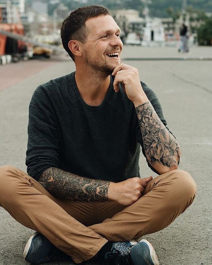 Igor Hush sitting on pavement with his hand on his chin and smiling with face inclined to the left.