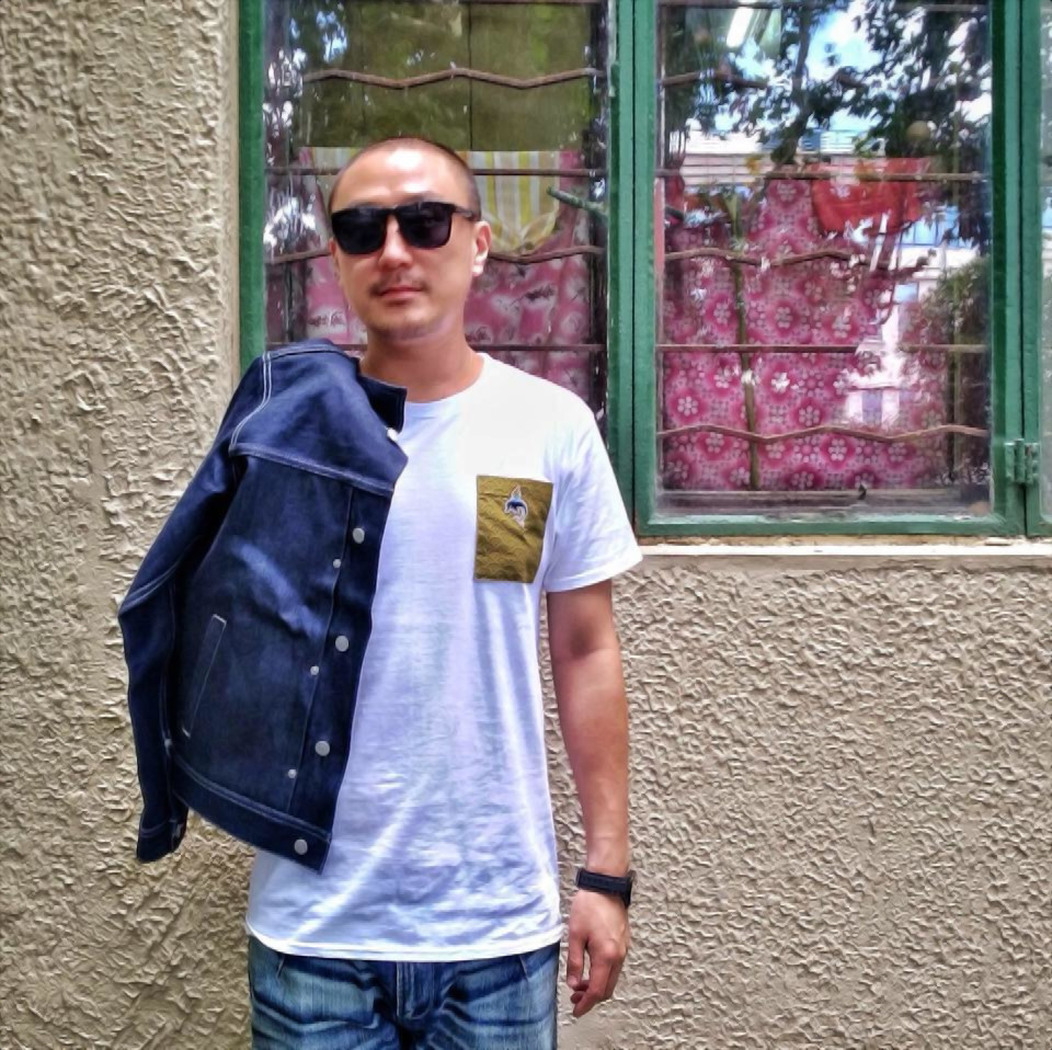 Taiwanese DJ and producer Murphy Kin standing in front of a window with his denim jacket over his right shoulder wearing Ray Ban sunglasses, colour image.