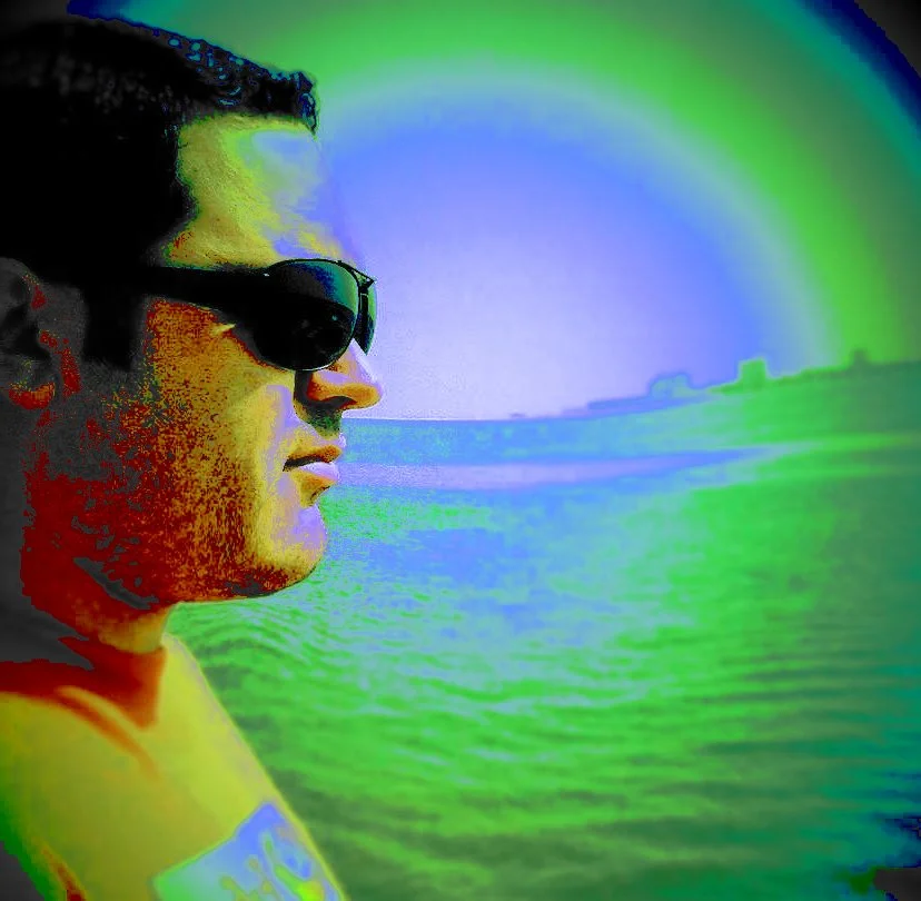 Portuguese DJ Joshua stands on the beach, wearing sunglasses and gazing to the left, captured in a colorful image with a swirling effect.