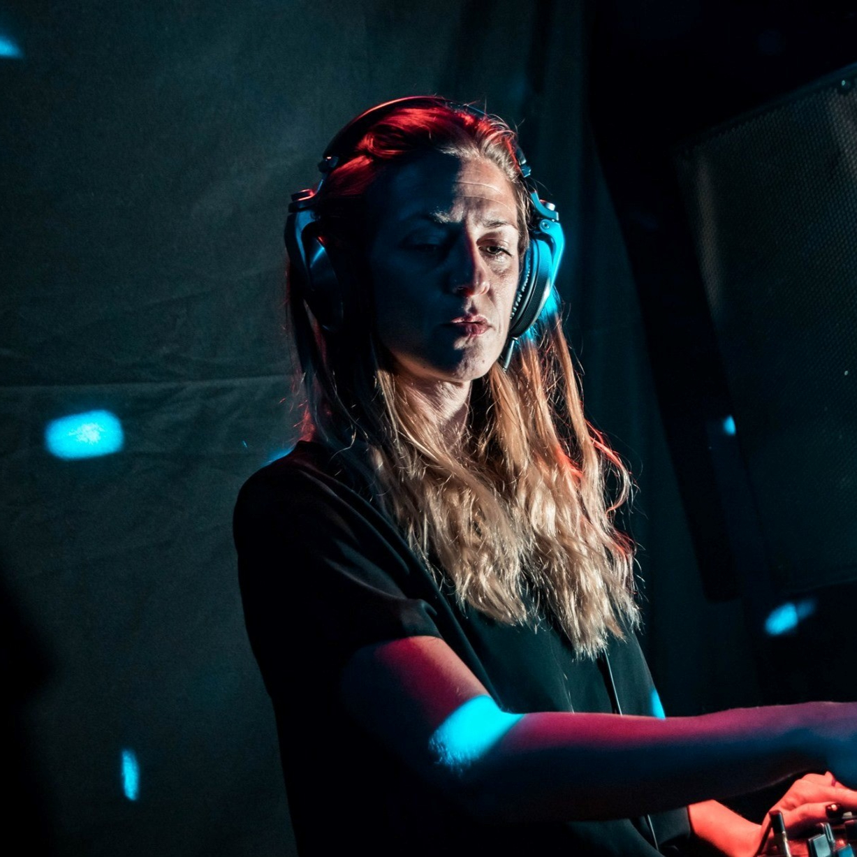 Argentinian DJ and producer Alma AR performing at an event wearing headphones, colour image.