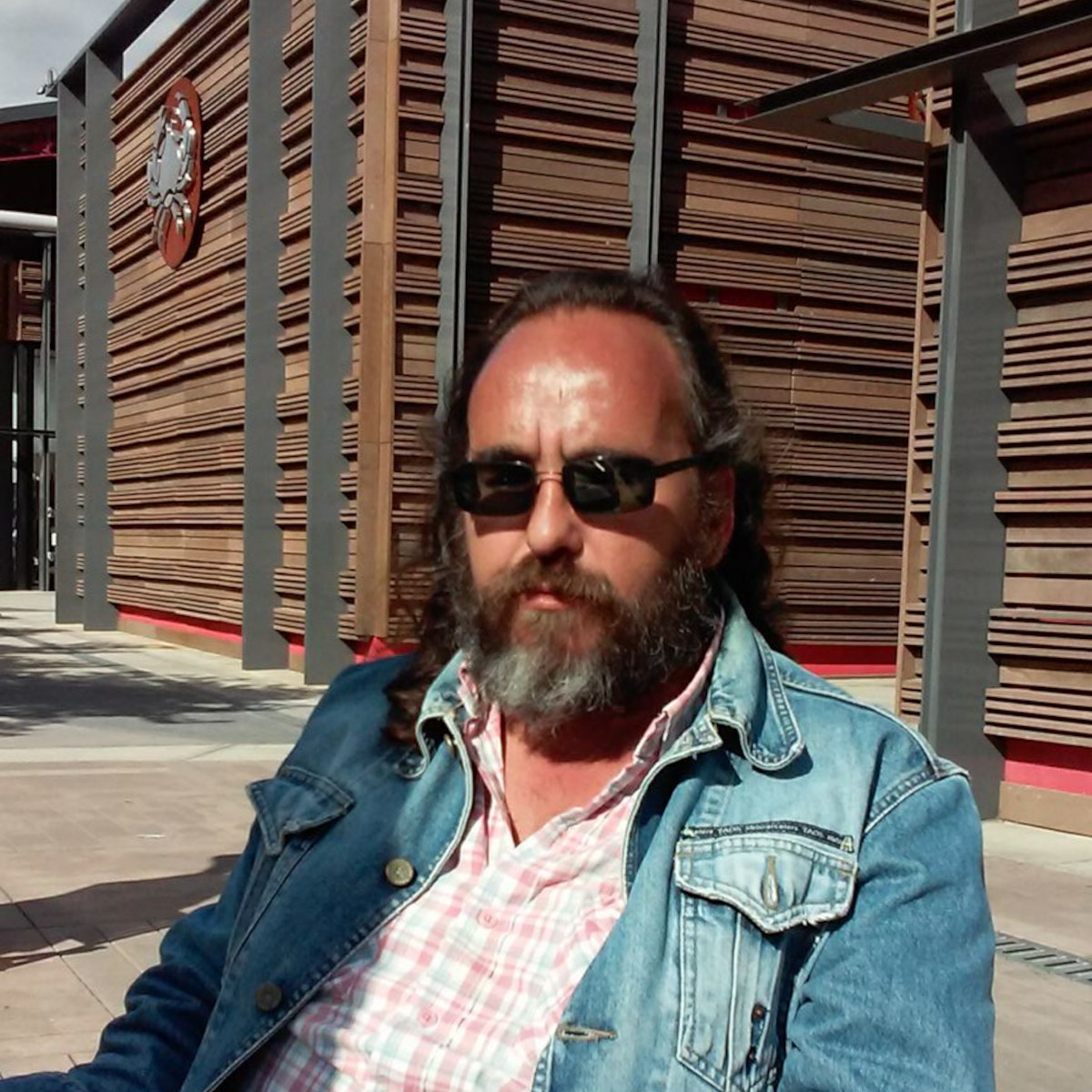 Argentinian DJ and producer Falso Simulacro sitting in a chair wearing sunglasses on a hot day, colour image.