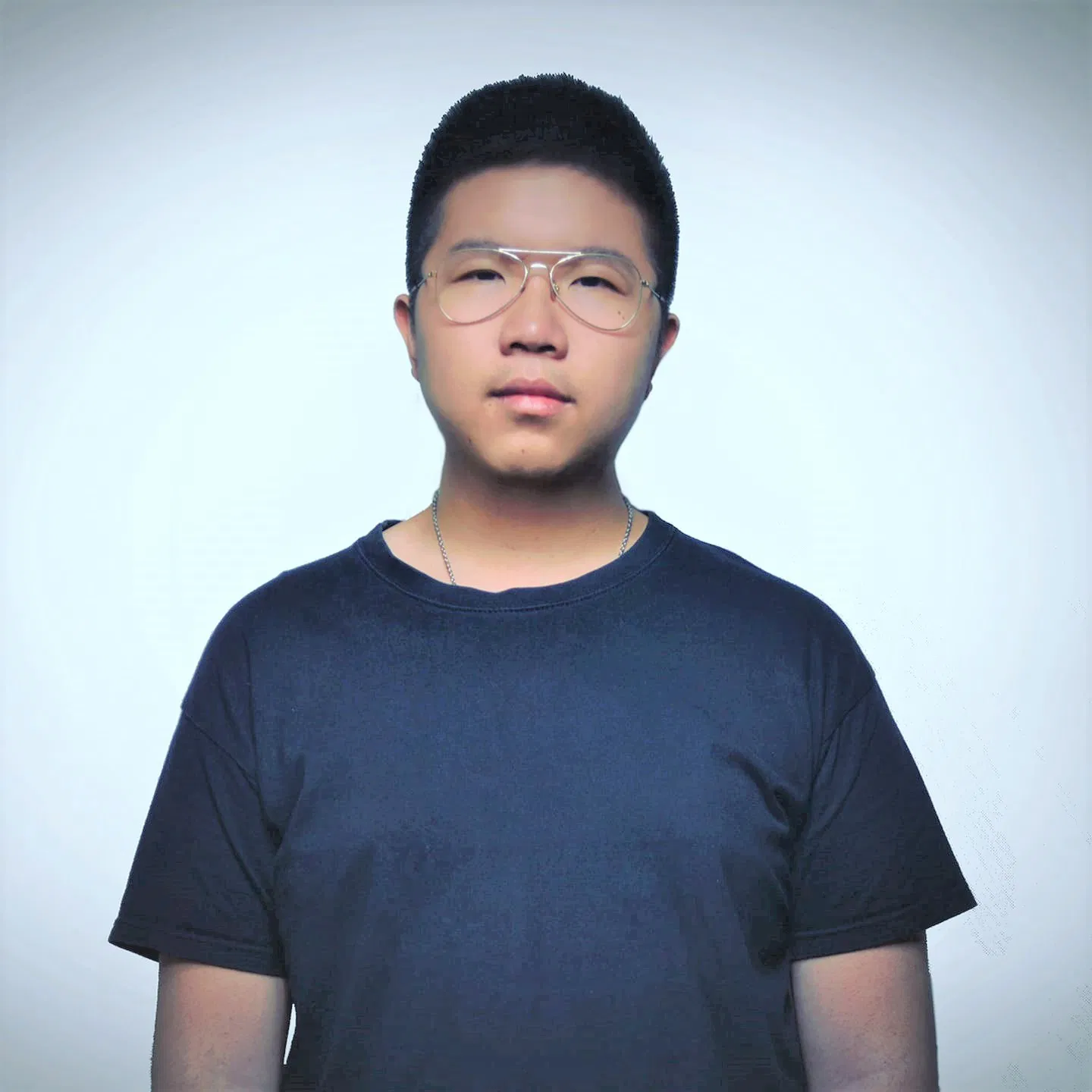 Guest DJ ToshShen wearing clear-framed glasses and a dark t-shirt, standing against a light background with soft lighting.
