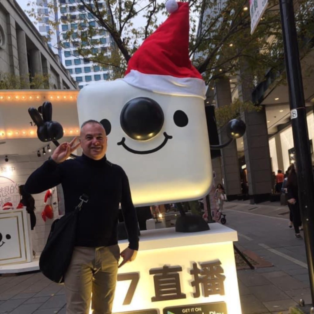 Italian DJ and producer Marco Mei standing in front of app robot wearing a Santa hat, colour image.