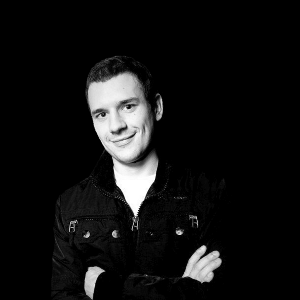 Russian DJ and Producer Alexander Filatov standing against a Black Background with arms folded whilst smiling.
