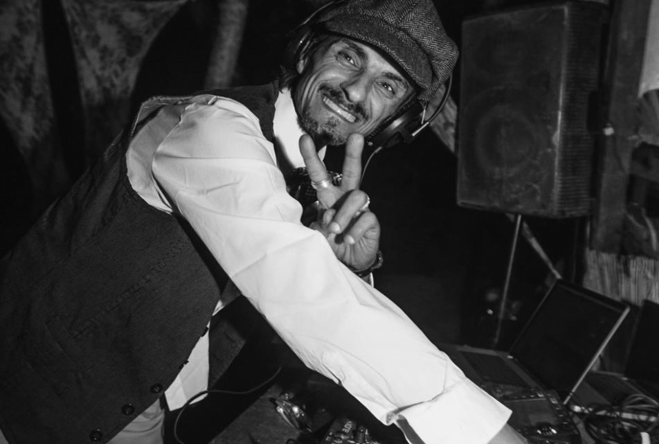 Italian DJ and producer Massimo Vivona performing as a DJ at an event looking at the camera and smiling, black and white image.