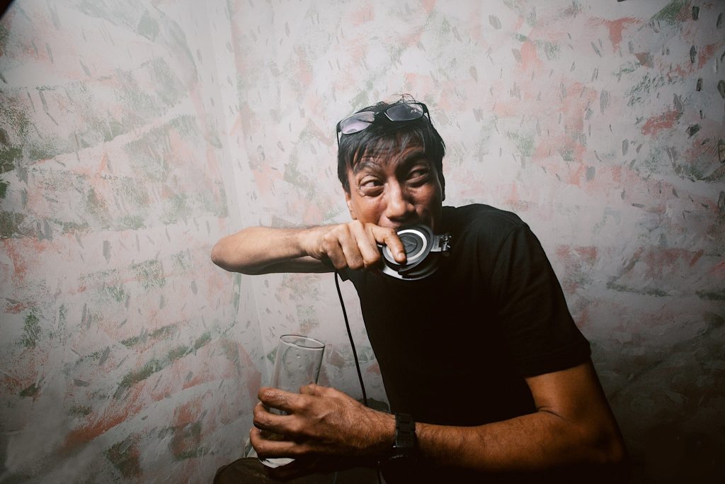 Singaporean DJ and producer Brendon P biting a headphone jokingly whilst holding a glass, colour image.