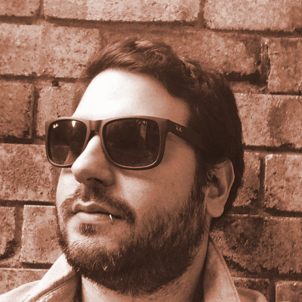 Argentinian DJ and producer Federico Puentes waering sunglasses and smirking with a toothpick in his mouth looking slightly right in headshot, black and white image with a brown tinge.