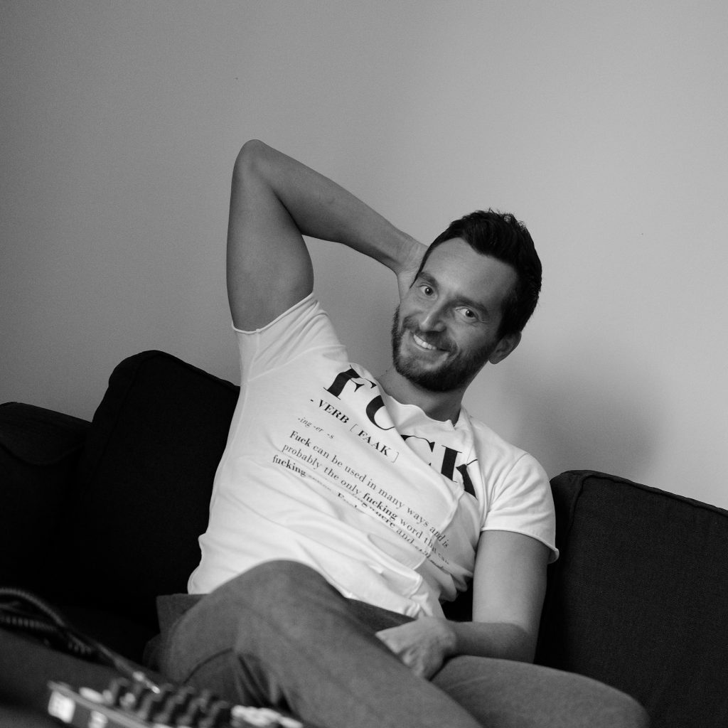 Italian DJ and Producer INVE of Italian Duo Inve and Forsi sitting on Sofa with hand behind head, black and white image.