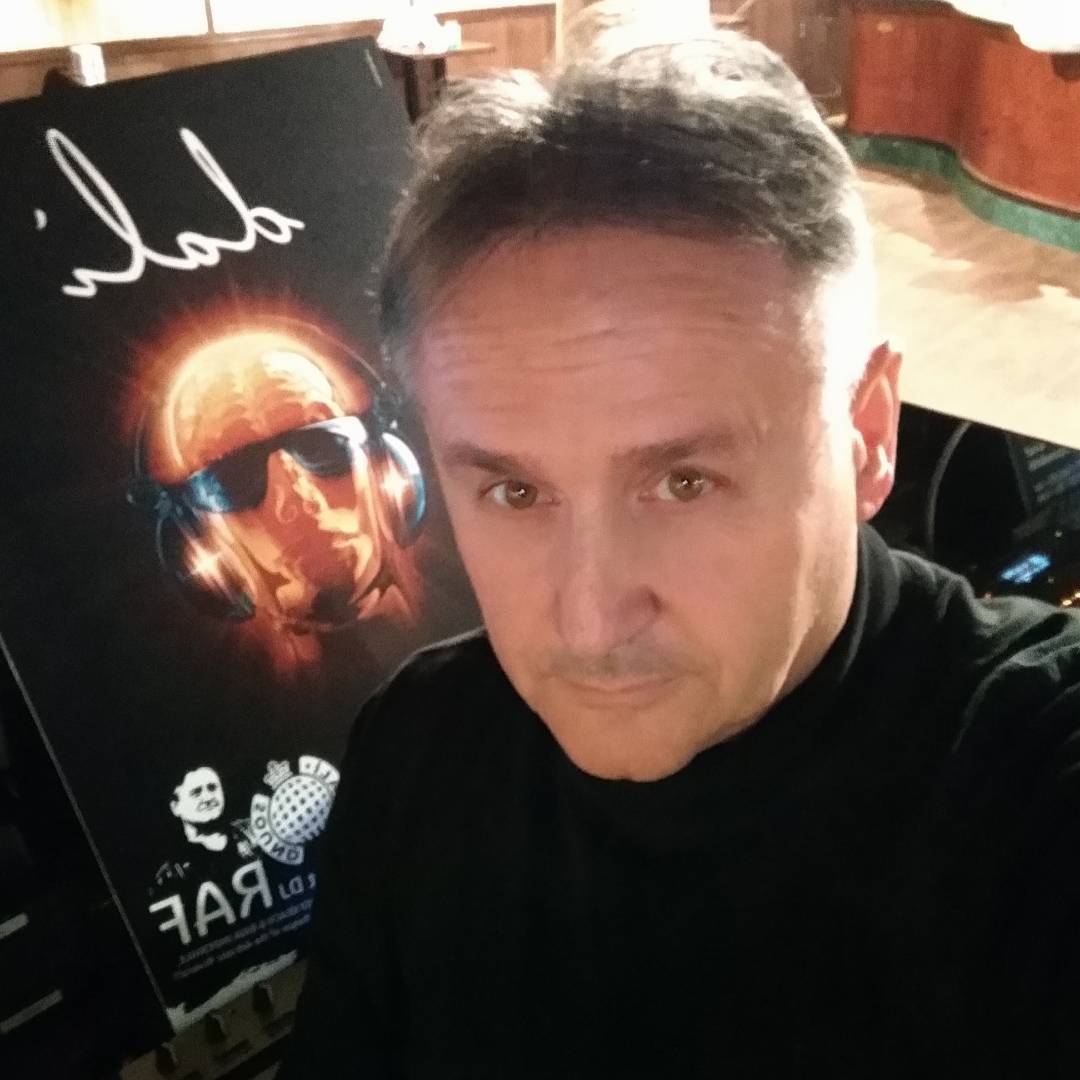 Italian DJ and Producer Raf standing in front of event poster.