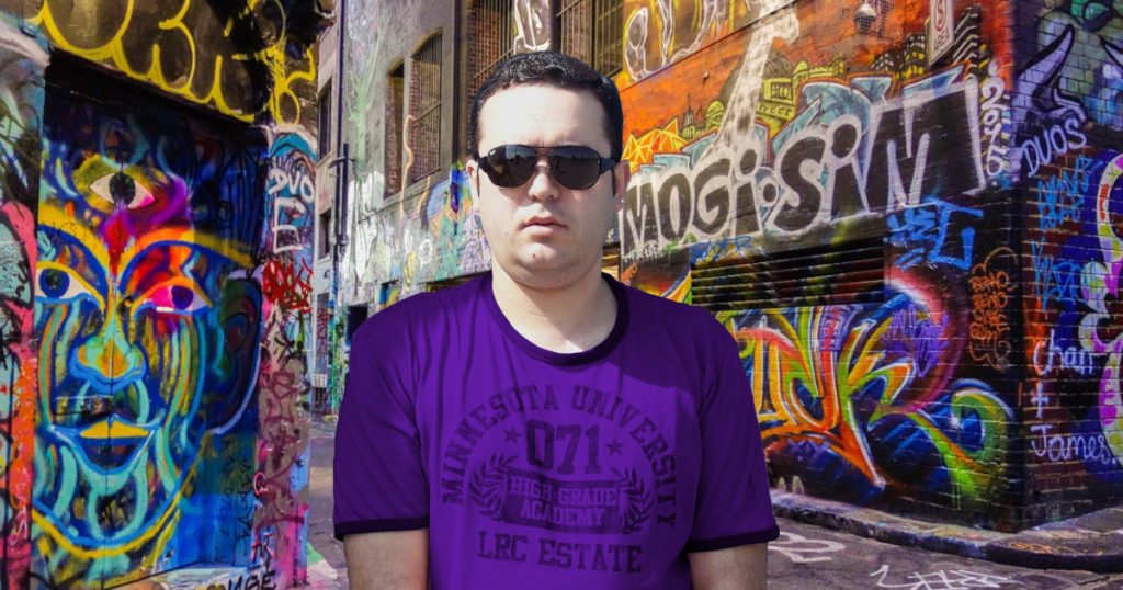 Portuguese DJ and producer Joshua stands on the corner of a graffiti-covered street, wearing sunglasses and a purple T-shirt, looking directly at the camera in a colourful image.