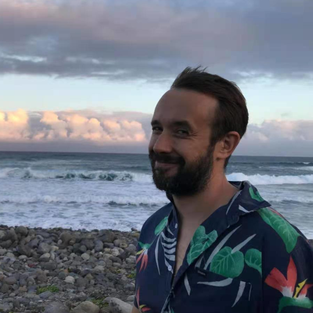 British DJ Chemical Oli standing on beach smiling at camera, colour image.