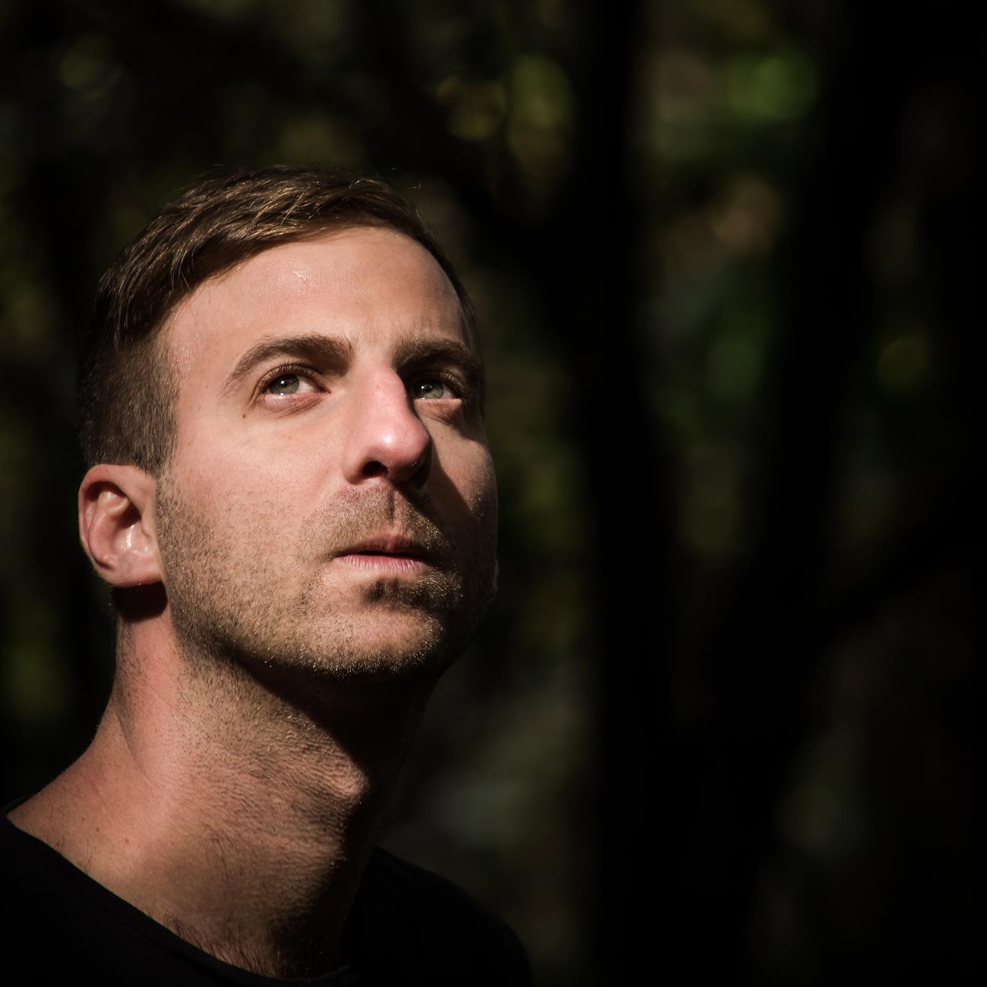 New Zealand based Agentinian DJ and producer Eichenbaum standing ouside looking up at the sky with some out of focus trees behind him, colour image.
