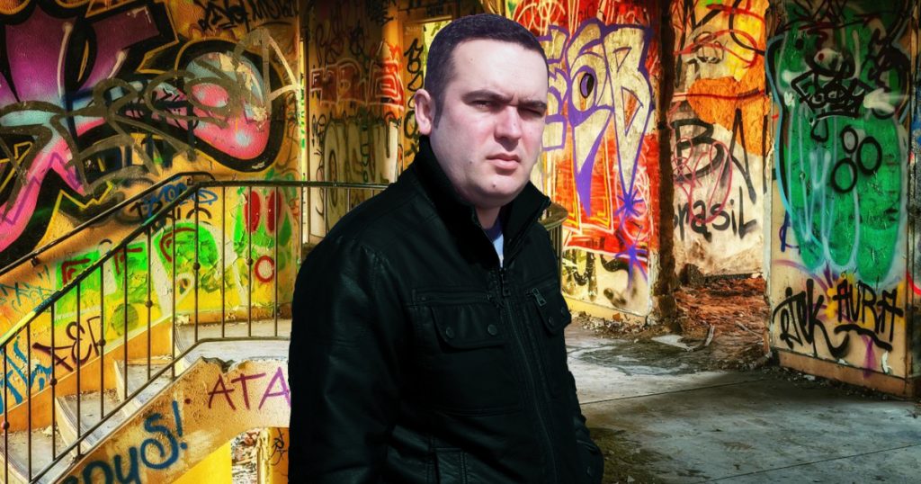Portuguese DJ Joshua standing in an abandoned building covered in graffiti, colour image.