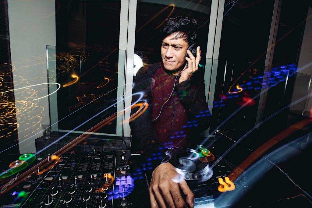 Singaporean DJ and producer Brendon P performing at Ce La Vi, Singapore with his left hand on his headphones, colour image with a swirl effect.