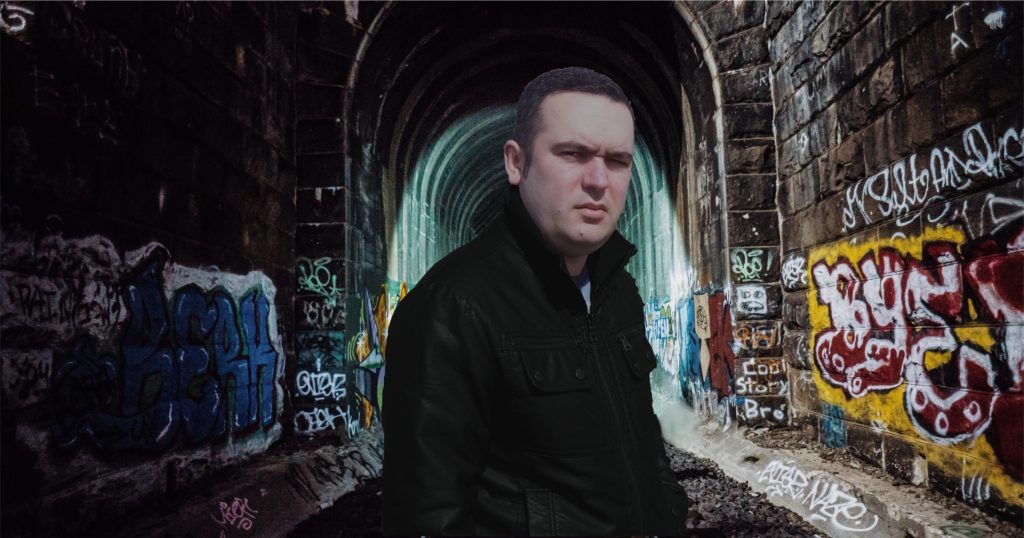 Portuguese DJ and producer Joshua standing on train track with Graffiti, colour image.