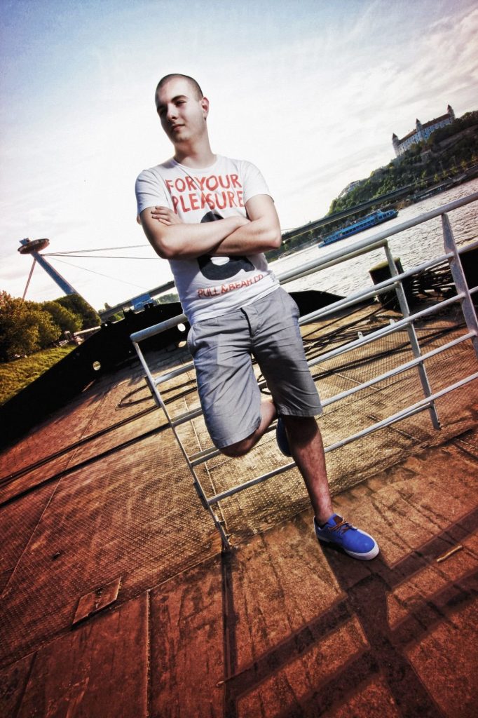 Slovakian DJ and producer Al Loudvoic standing leaning against rail with arms crossed.