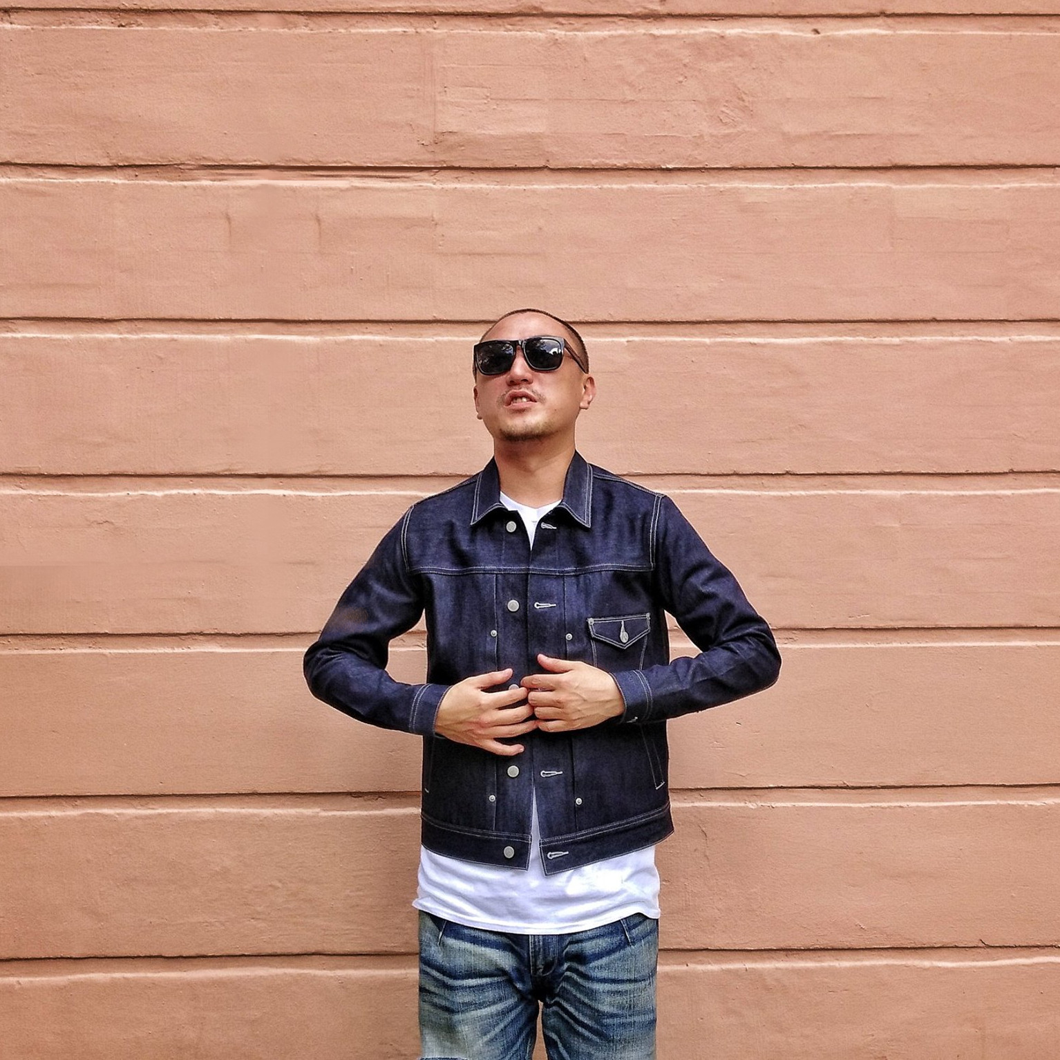 Taiwanese DJ and producer Murphy Kin standing against a wall wearing shades and a denim jacket, colour image.