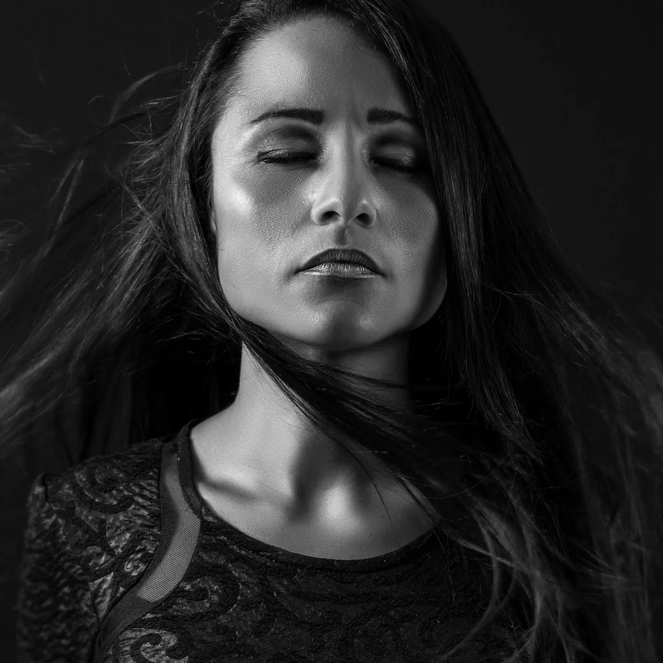Guest DJ Grasi Francis in a black and white portrait, eyes closed with wind-blown hair, wearing a textured dark top against a dark studio background.