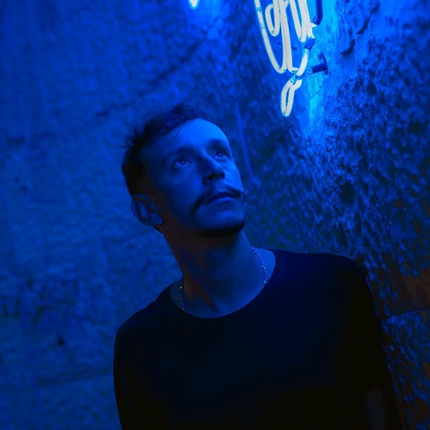 Argentinian DJ and producer Gusti Rabago standing under a blue neon light, colour image.