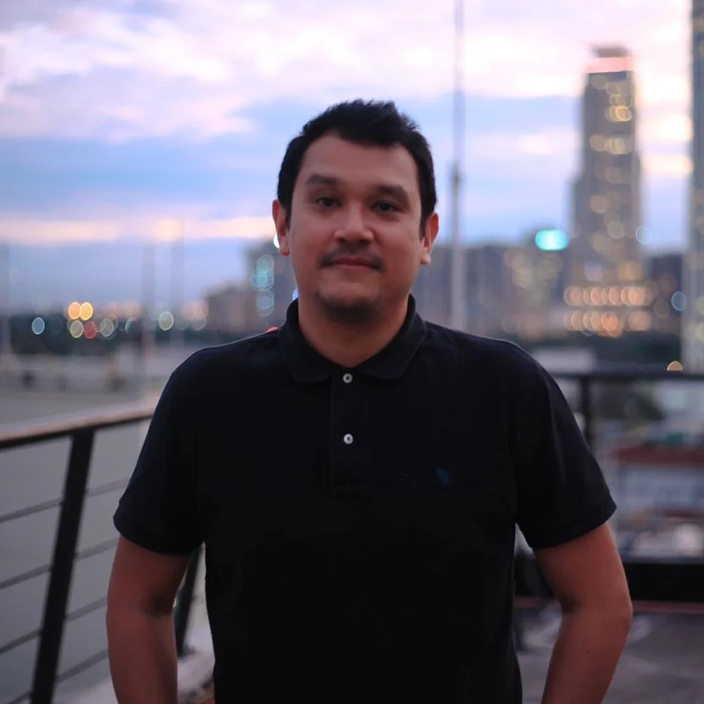 Filipino DJ Cao Ocampo standing on a roof in Manila looking at cfamera, colour image.