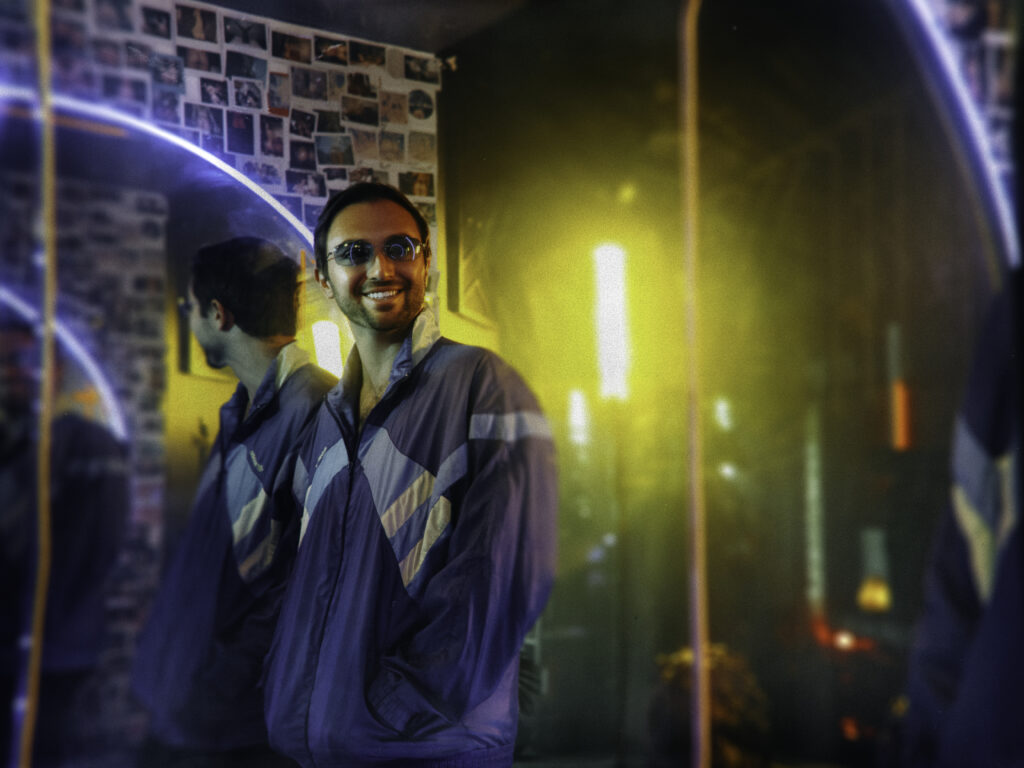 DJ Eddy Palermo photographed in a colourful, neon-lit club setting.