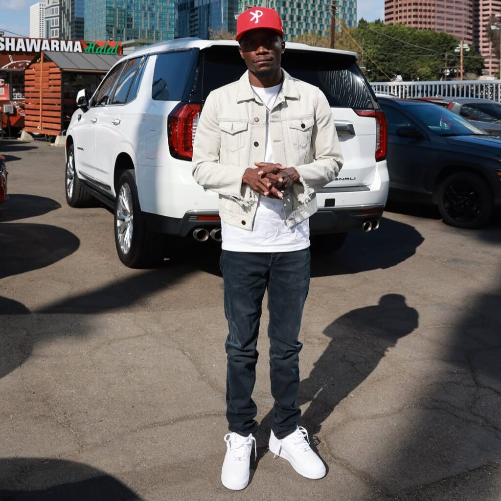 Philadelphia rapper Fakefree KP pictured outdoors in a red cap and light denim jacket.