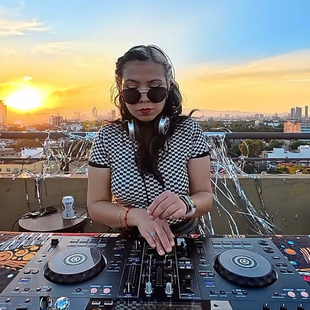 DJ Blitsize DJing at sunset during a rooftop electronic music performance.