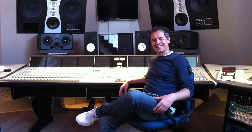 Italian DJ Ezio Vallini, known as DJ Valez, seated in a recording studio in front of a large mixing console.