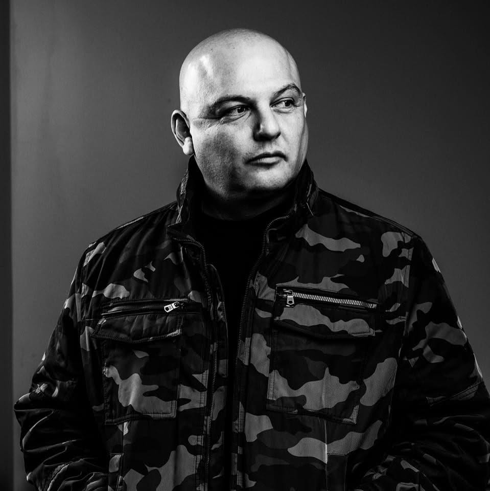 American Hip Hop artist Mic Bles from Oxnard, California, wearing a camouflage jacket and looking to his left in a black-and-white studio portrait.